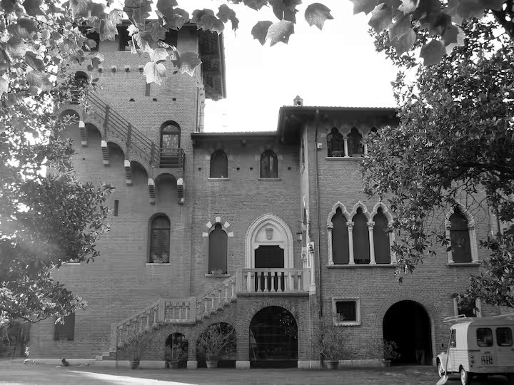 A brick villa with a tower and stone entrance terrace, seen across the lawn